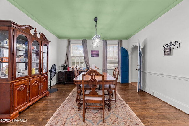 dining space with ornamental molding, arched walkways, dark wood finished floors, and baseboards