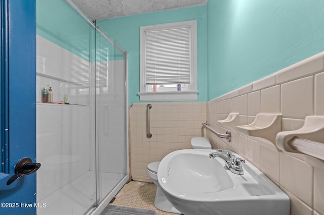 full bath featuring toilet, a sink, a textured ceiling, a shower stall, and tile walls