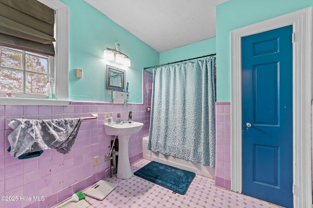 bathroom with a wainscoted wall, a sink, tile walls, and shower / bathtub combination with curtain