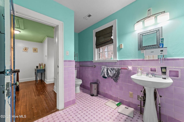 bathroom featuring visible vents, wainscoting, toilet, and tile walls