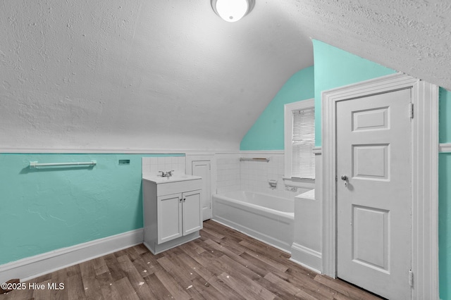 full bathroom with wood finished floors, a garden tub, vaulted ceiling, a textured ceiling, and vanity