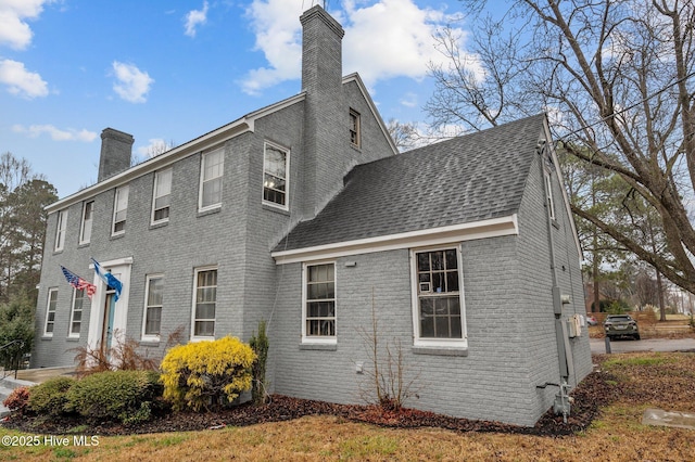 view of property exterior with roof with shingles, a chimney, and brick siding