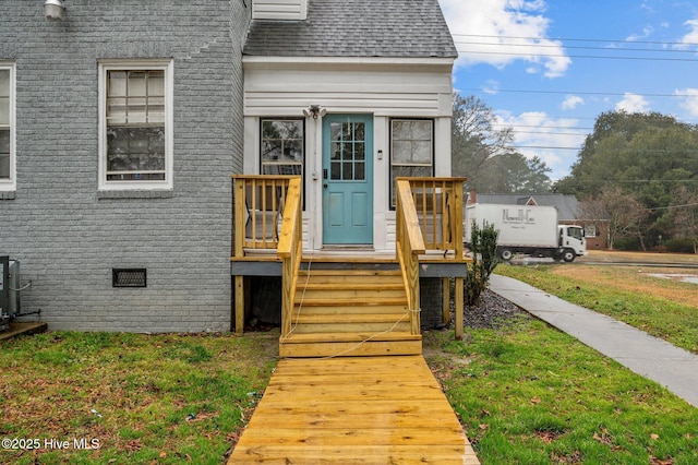 entrance to property with a yard, crawl space, roof with shingles, and brick siding