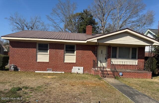 view of front facade featuring metal roof, brick siding, a front lawn, and a chimney