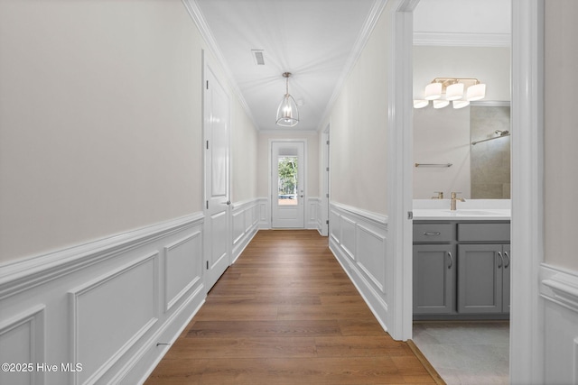 corridor with wood finished floors, a sink, ornamental molding, and a decorative wall