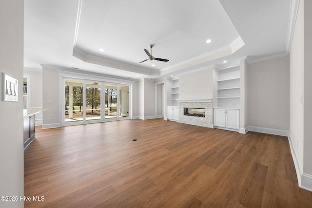 unfurnished living room featuring a raised ceiling, wood finished floors, ceiling fan, and a fireplace