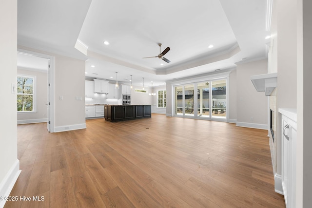 unfurnished living room with ornamental molding, ceiling fan, a raised ceiling, and a fireplace