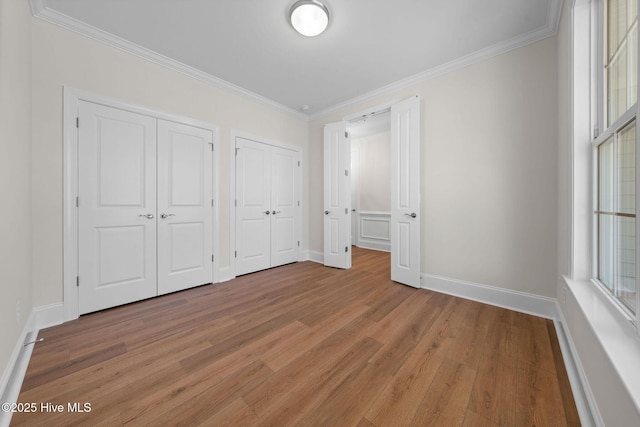 unfurnished bedroom with light wood-type flooring, crown molding, baseboards, and multiple closets