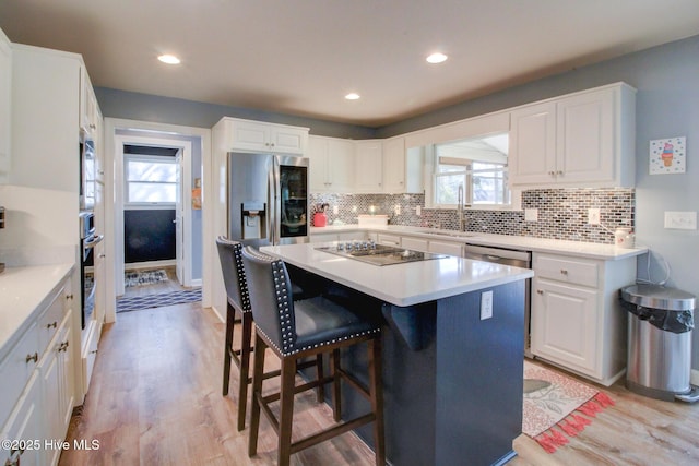 kitchen with appliances with stainless steel finishes, a breakfast bar, a sink, light wood-type flooring, and backsplash