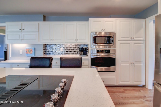 kitchen featuring white cabinets, light wood finished floors, stainless steel appliances, and decorative backsplash