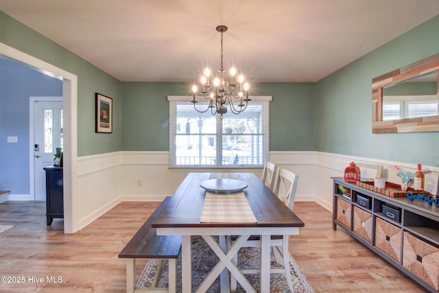 dining room featuring light wood-type flooring, a wainscoted wall, and a notable chandelier