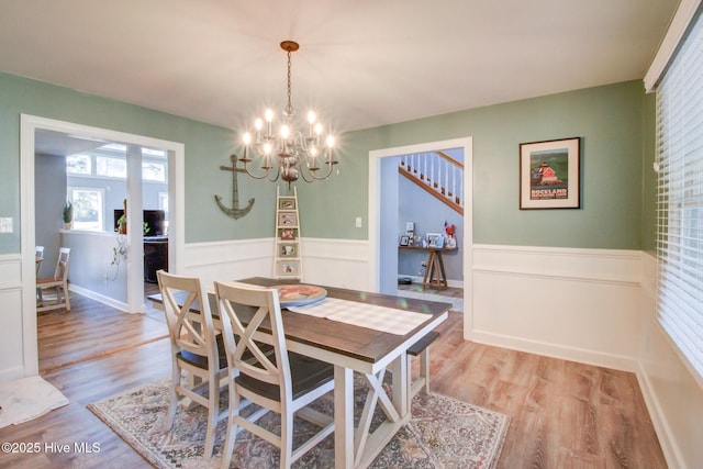 dining space with a wainscoted wall, light wood-style flooring, and an inviting chandelier