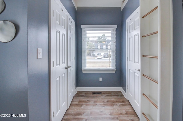 corridor with light wood-type flooring, baseboards, and visible vents