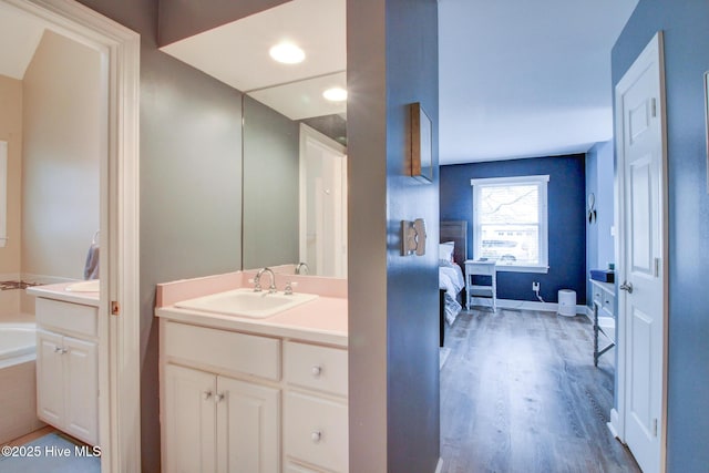 ensuite bathroom with connected bathroom, vanity, a bath, and wood finished floors