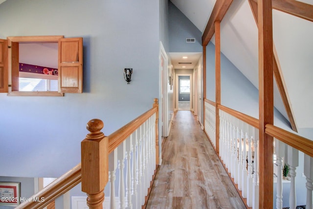 hallway featuring light wood-style floors, lofted ceiling, visible vents, and an upstairs landing