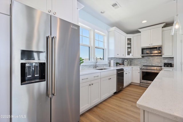 kitchen featuring white cabinets, a sink, stainless steel appliances, light wood-type flooring, and tasteful backsplash