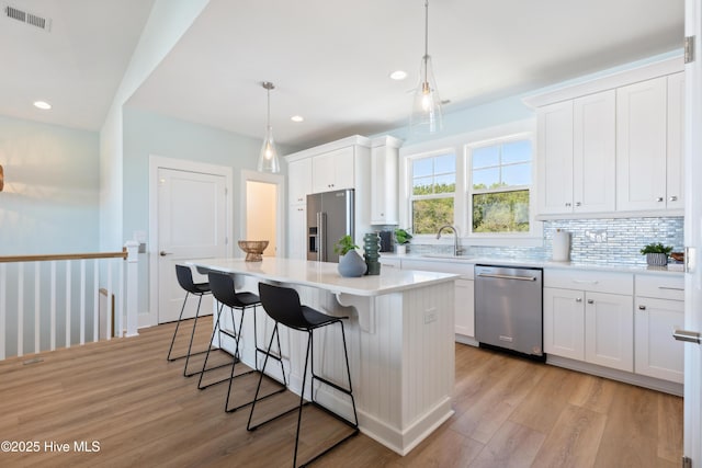 kitchen with visible vents, appliances with stainless steel finishes, light wood-style floors, a kitchen bar, and a sink