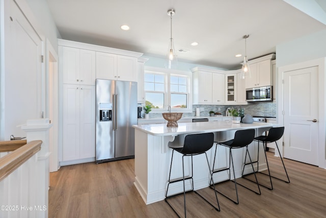 kitchen with light wood-type flooring, light countertops, glass insert cabinets, stainless steel appliances, and white cabinetry