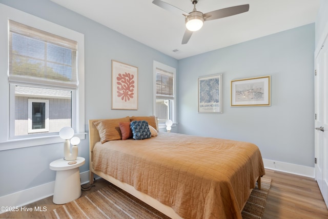 bedroom with a ceiling fan, visible vents, baseboards, and wood finished floors