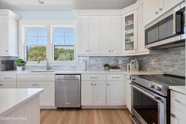 kitchen featuring light stone counters, stainless steel appliances, decorative backsplash, light wood-style floors, and a sink