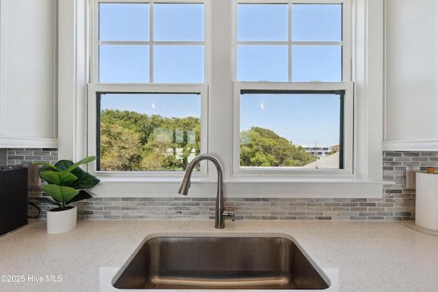 room details featuring a sink, tasteful backsplash, light stone countertops, and white cabinetry