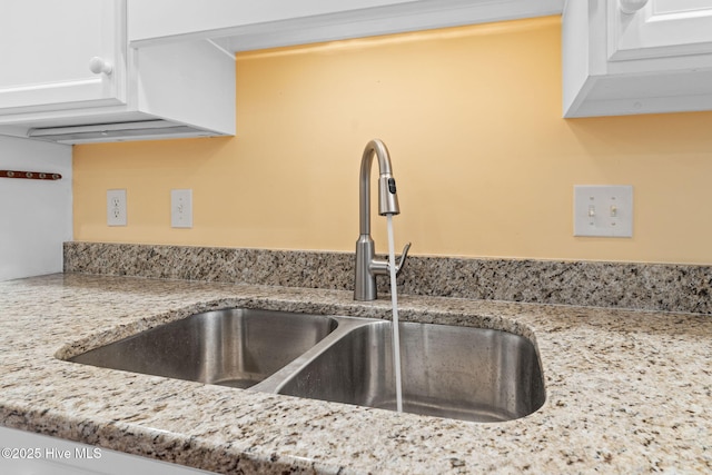 interior details with sink, light stone countertops, and white cabinets