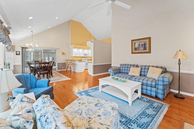 living room with ceiling fan with notable chandelier, high vaulted ceiling, and light wood-type flooring