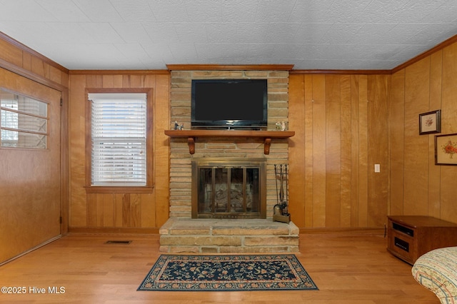 living room with a large fireplace, visible vents, wood walls, and wood finished floors