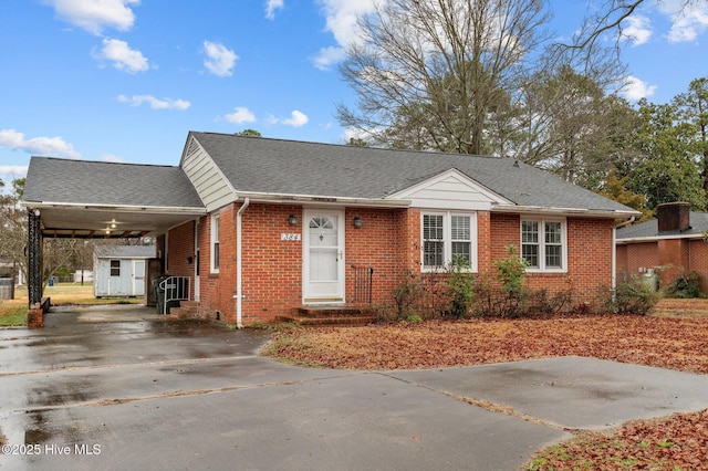 view of front of house with brick siding, a shingled roof, concrete driveway, a carport, and an outdoor structure