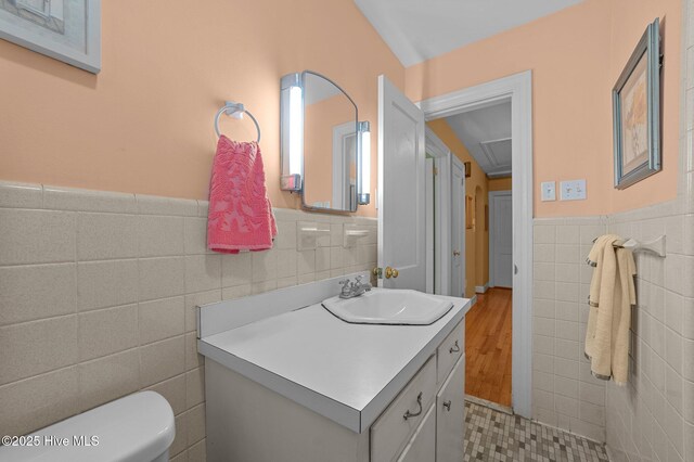 half bathroom featuring toilet, vanity, tile walls, and wainscoting