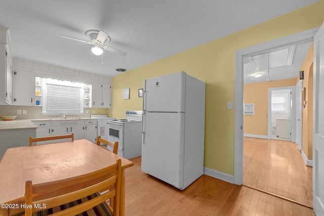 kitchen featuring light wood-style flooring, white appliances, a sink, visible vents, and light countertops