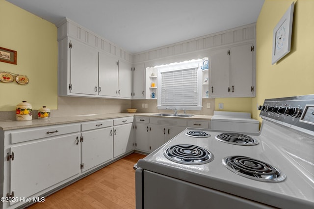 kitchen with range with electric stovetop, light countertops, white cabinets, a sink, and light wood-type flooring