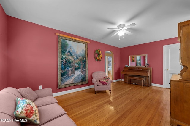 sitting room with arched walkways, light wood finished floors, a ceiling fan, and baseboards