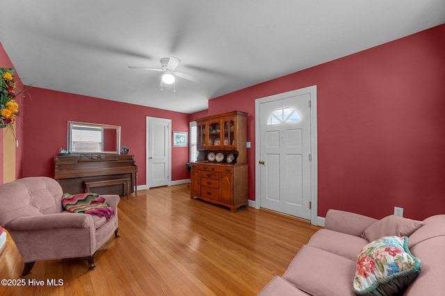 living area featuring a ceiling fan, light wood-style flooring, and baseboards