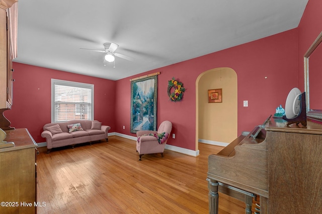 living area with light wood-type flooring, ceiling fan, arched walkways, and baseboards