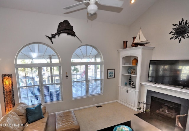 carpeted living area with visible vents, baseboards, a ceiling fan, a fireplace with flush hearth, and high vaulted ceiling