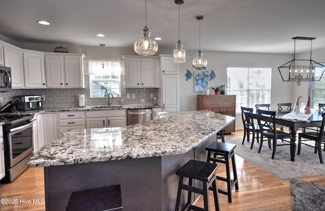 kitchen with tasteful backsplash, white cabinets, appliances with stainless steel finishes, light wood-style floors, and a sink