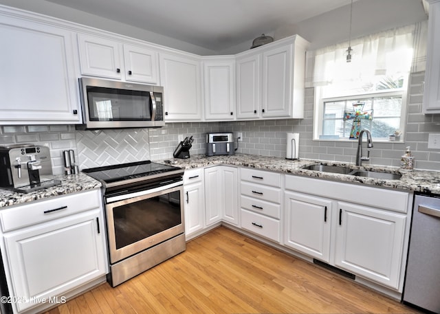 kitchen with stainless steel appliances, white cabinetry, a sink, and light wood-style flooring