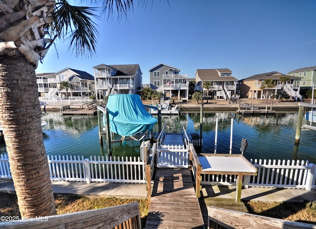 view of dock featuring boat lift, a water view, fence, and a residential view