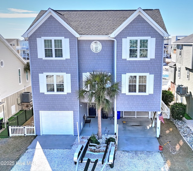 view of front of property with central AC unit, concrete driveway, roof with shingles, an attached garage, and fence