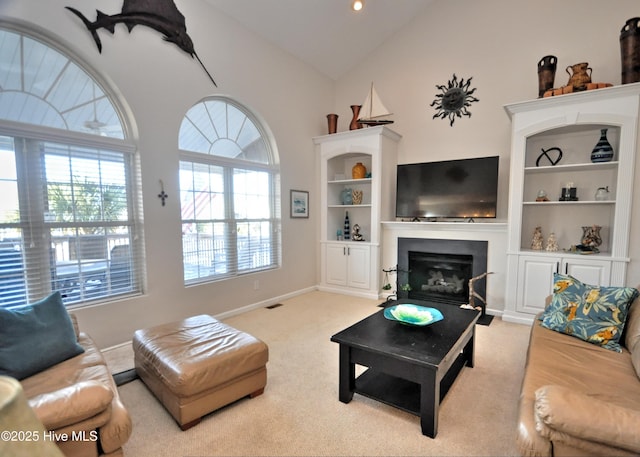 carpeted living area with visible vents, high vaulted ceiling, baseboards, and a glass covered fireplace