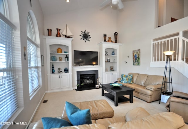 carpeted living room featuring ceiling fan, high vaulted ceiling, a fireplace with flush hearth, visible vents, and baseboards