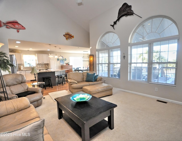 living room featuring recessed lighting, light colored carpet, visible vents, high vaulted ceiling, and baseboards