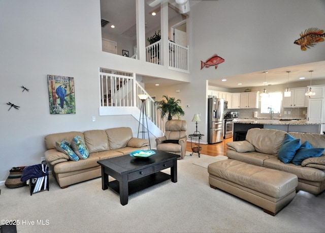 living area featuring recessed lighting, visible vents, stairway, and a towering ceiling