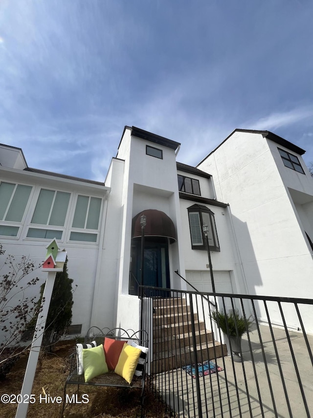 view of front facade with stucco siding, an attached garage, and fence