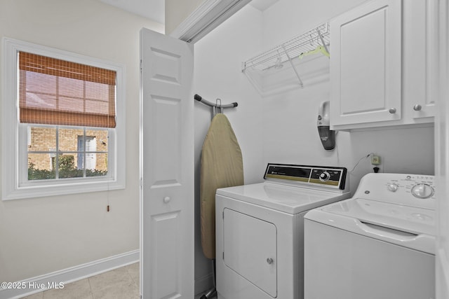 clothes washing area featuring light tile patterned flooring, washing machine and clothes dryer, cabinet space, and baseboards