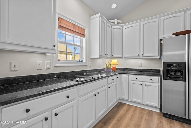 kitchen featuring dark stone counters, stainless steel refrigerator with ice dispenser, white cabinetry, and black electric cooktop