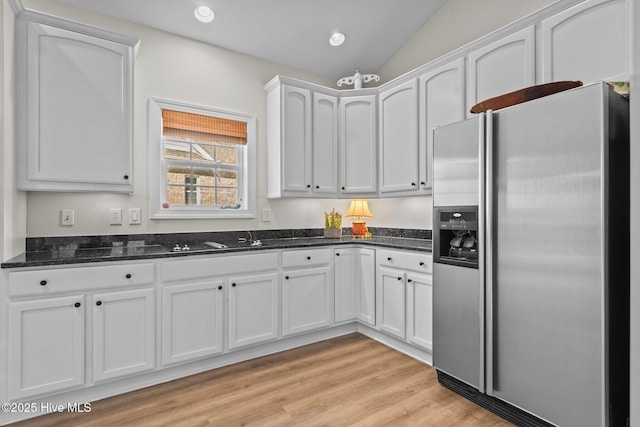 kitchen with stainless steel refrigerator with ice dispenser, recessed lighting, light wood-style flooring, white cabinets, and dark stone counters