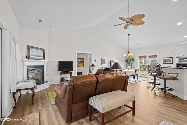 living room featuring high vaulted ceiling, ceiling fan with notable chandelier, a premium fireplace, visible vents, and light wood-type flooring