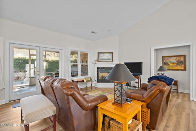 living area featuring lofted ceiling, light wood-type flooring, a high end fireplace, and visible vents